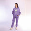 Person wearing a purple hoodie and pants with a cat face on a light pink background