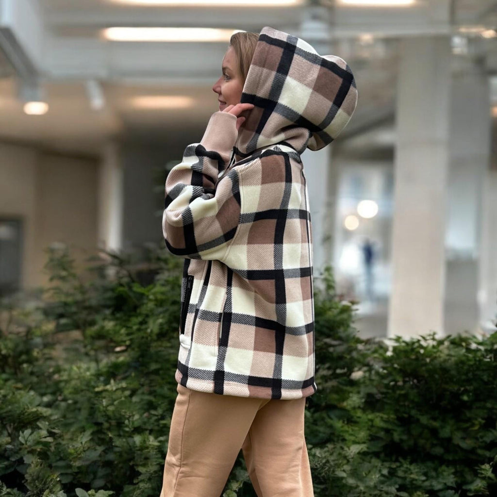 Person wearing a Beige plaid hoodie in an indoor setting with plants and a blurred background