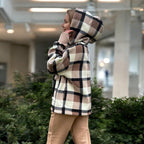 Person wearing a Beige plaid hoodie in an indoor setting with plants and a blurred background