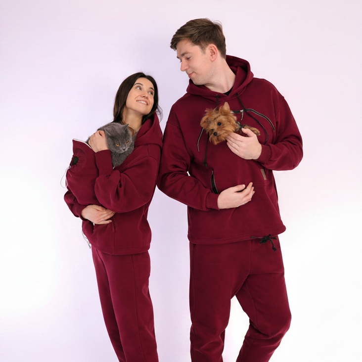 Two people wearing matching  Burgundy sets holding small dog and cat on a white background
