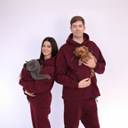 Two people wearing matching  Burgundy outfits holding a cat and a dog on a white background
