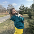 Person holding a cat outdoors with trees and road in the background