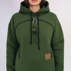 An dark green pullover hoodie with a unique circular chest design, black drawstrings, and a small brown leather patch on the front pocket, shown on a model.