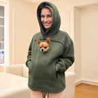 Person wearing a Khaki Sherpa hoodie with a dog peeking out of the front pocket, standing in a room.