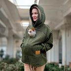 Person wearing a Khaki Sherpa hoodie with a pocket containing a cat, standing indoors.