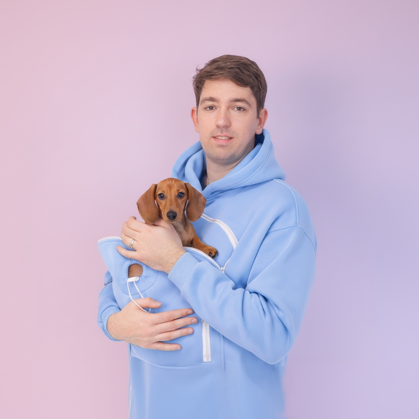 Man in a Light Blue hoodie holding a small brown dog against a light purple background