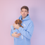Man in a Light Blue hoodie holding a small brown dog against a light purple background