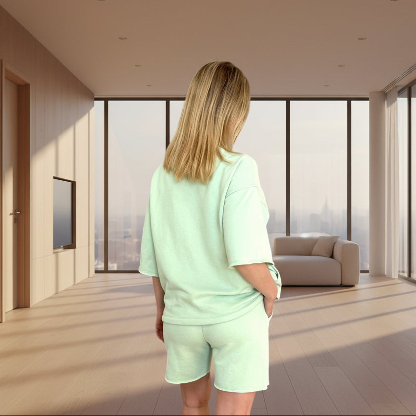 Person wearing a lime green outfit standing in a modern room with large windows.