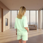 Person wearing a lime green outfit standing in a modern room with large windows.