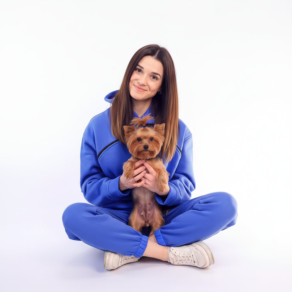Woman in Royal Blue tracksuit holding a small brown dog on a white background