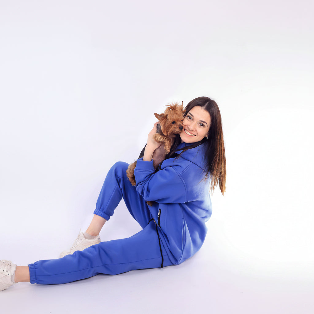 Woman in a Royal Blue tracksuit holding a small dog on a white background Main image