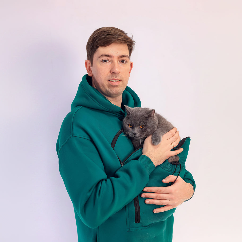 Man in teal hoodie holding a gray cat against a white background