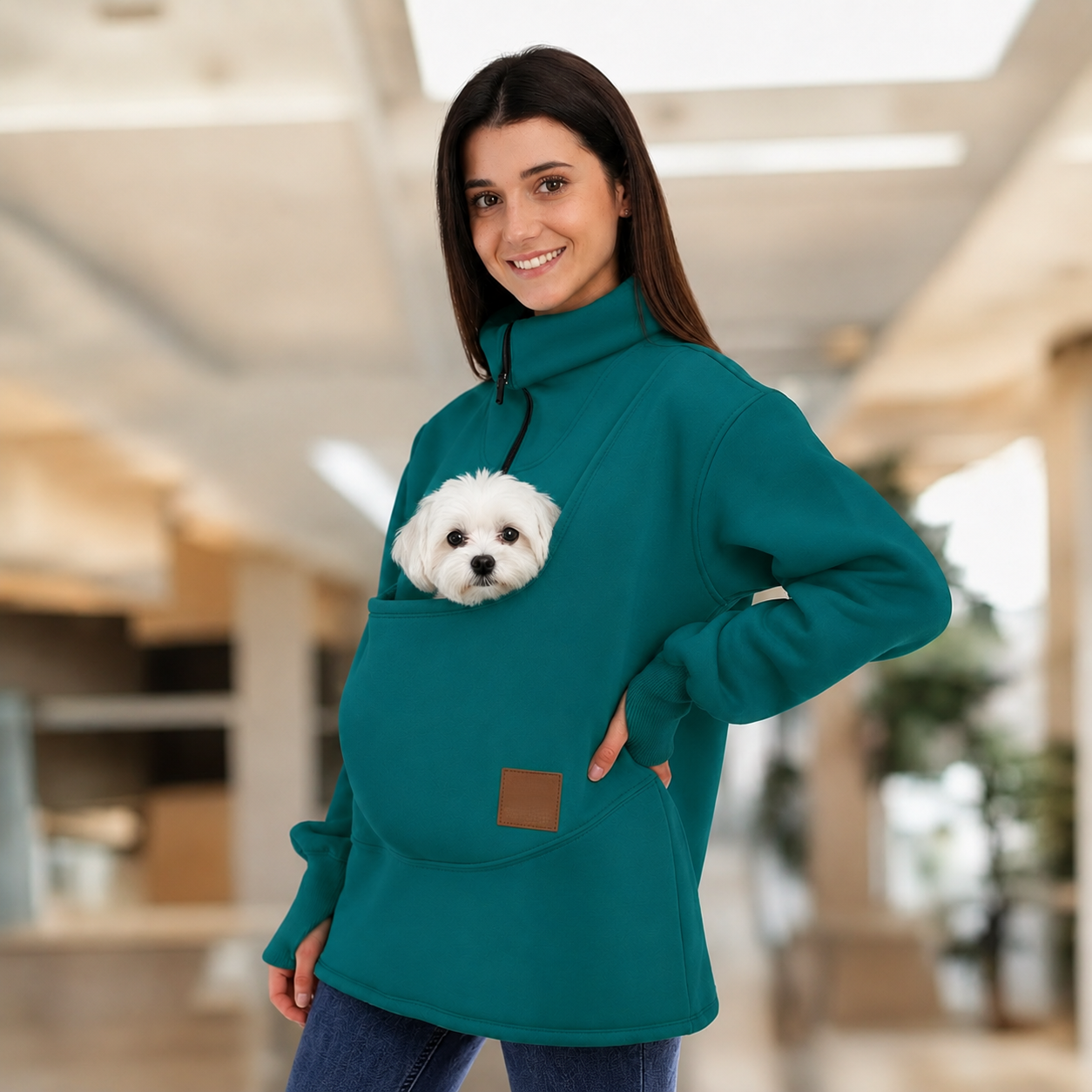 Women wearing a teal sweatshirt with a dog in pouch, standing indoors. Main image