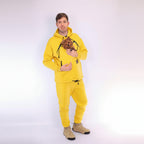 Men wearing a yellow hoodie and matching pants holding a small dog on a white background