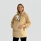 Person wearing a beige boucle hoodie with a pocket containing a small white dog on a light purple background