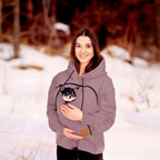 Woman wearing a beige hoodie with a small dog plush toy in a snowy outdoor setting