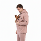 Man in beige  tracksuit holding a small dog on a white background