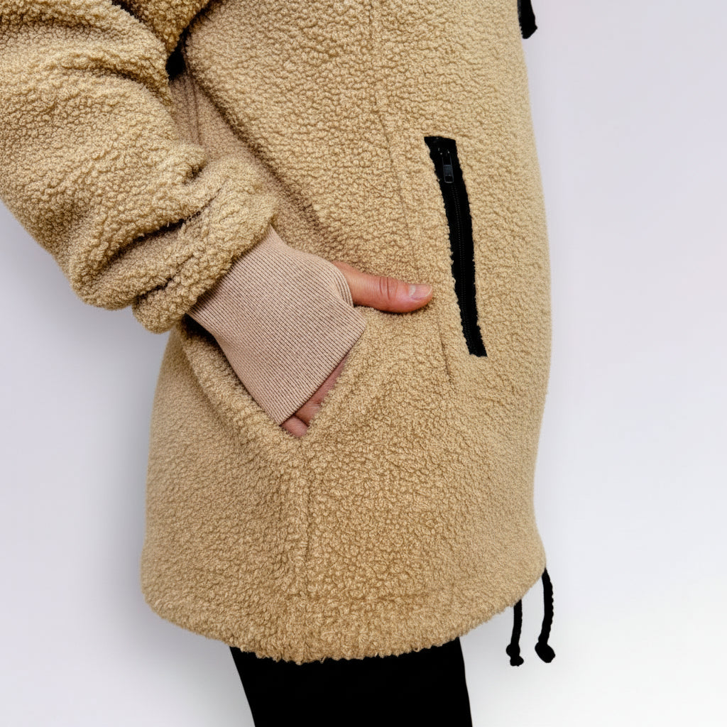 Beige sherpa hoodie with a hand peeking out from a pocket on a white background