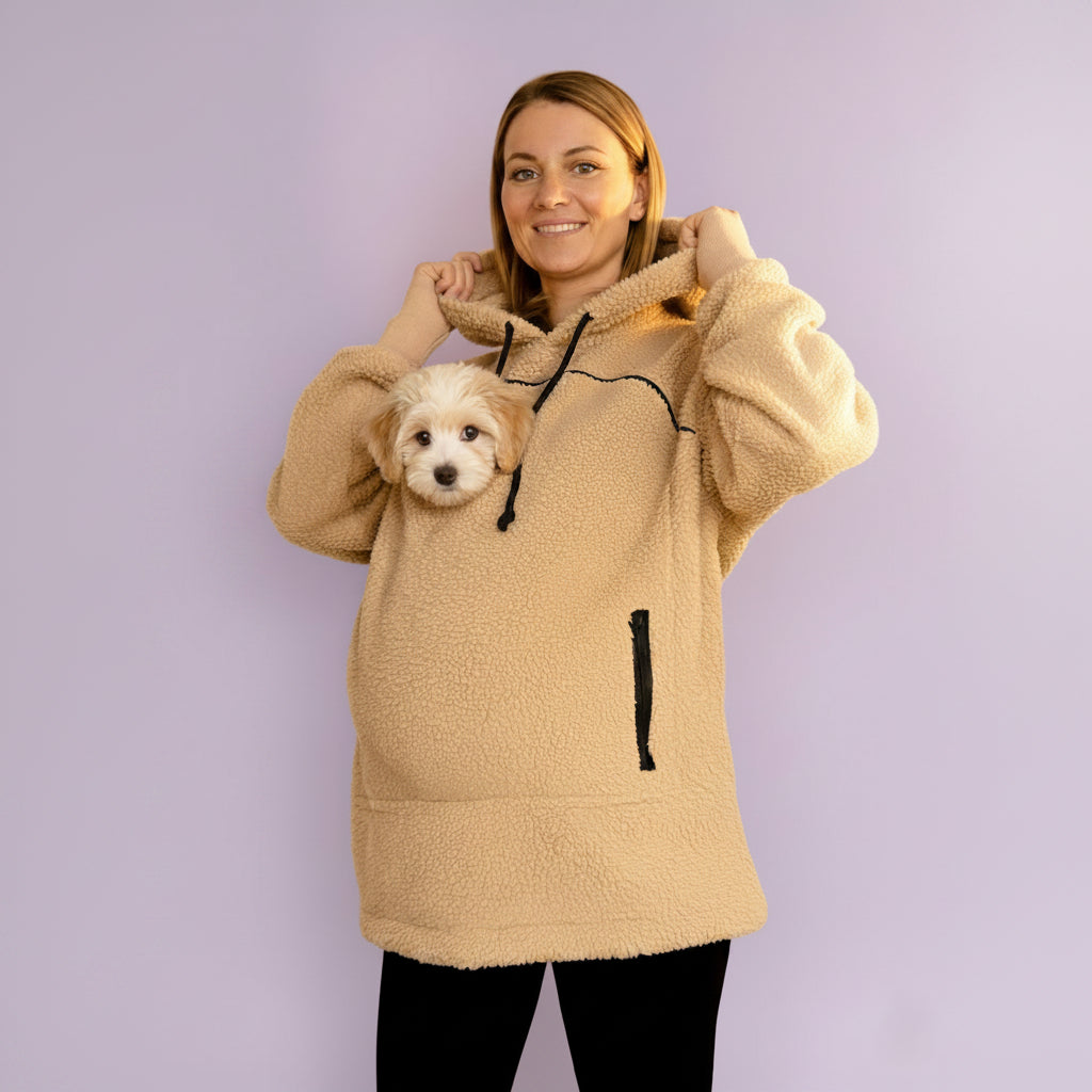 Person wearing a beige boucle fleece hoodie with a small dog peeking out from inside, against a light purple background