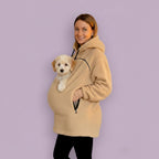 Person wearing a beige boucle hoodie with a pocket holding a small dog against a purple background