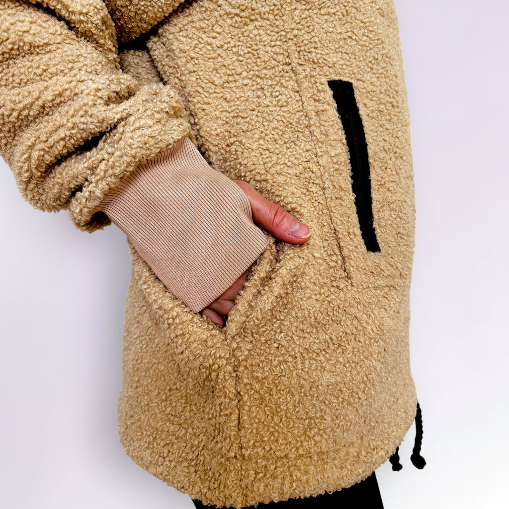Close-up of a person wearing a beige boucle sherpa jacket with a white background