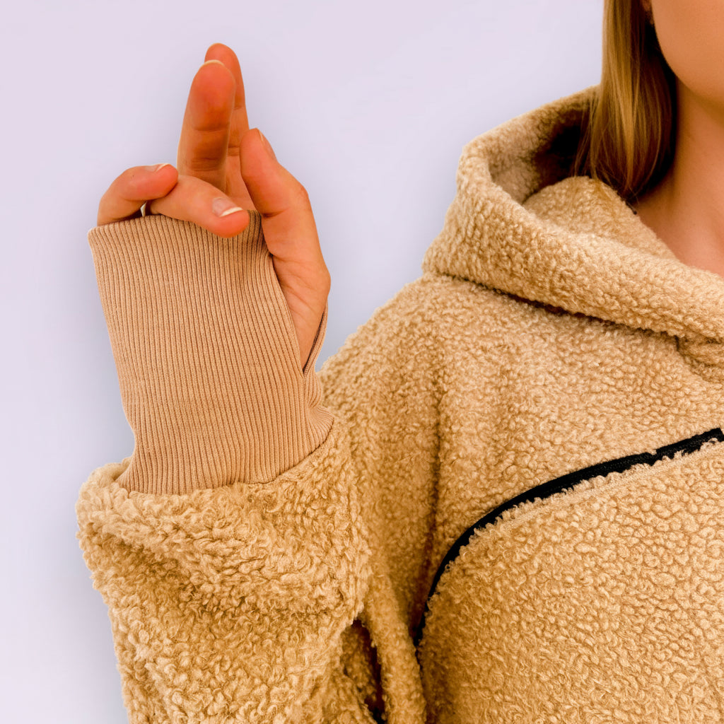 Close-up of a person wearing a beige boucle fleece jacket with a plain background