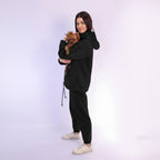 Woman in black tracksuit holding a small dog on a white background