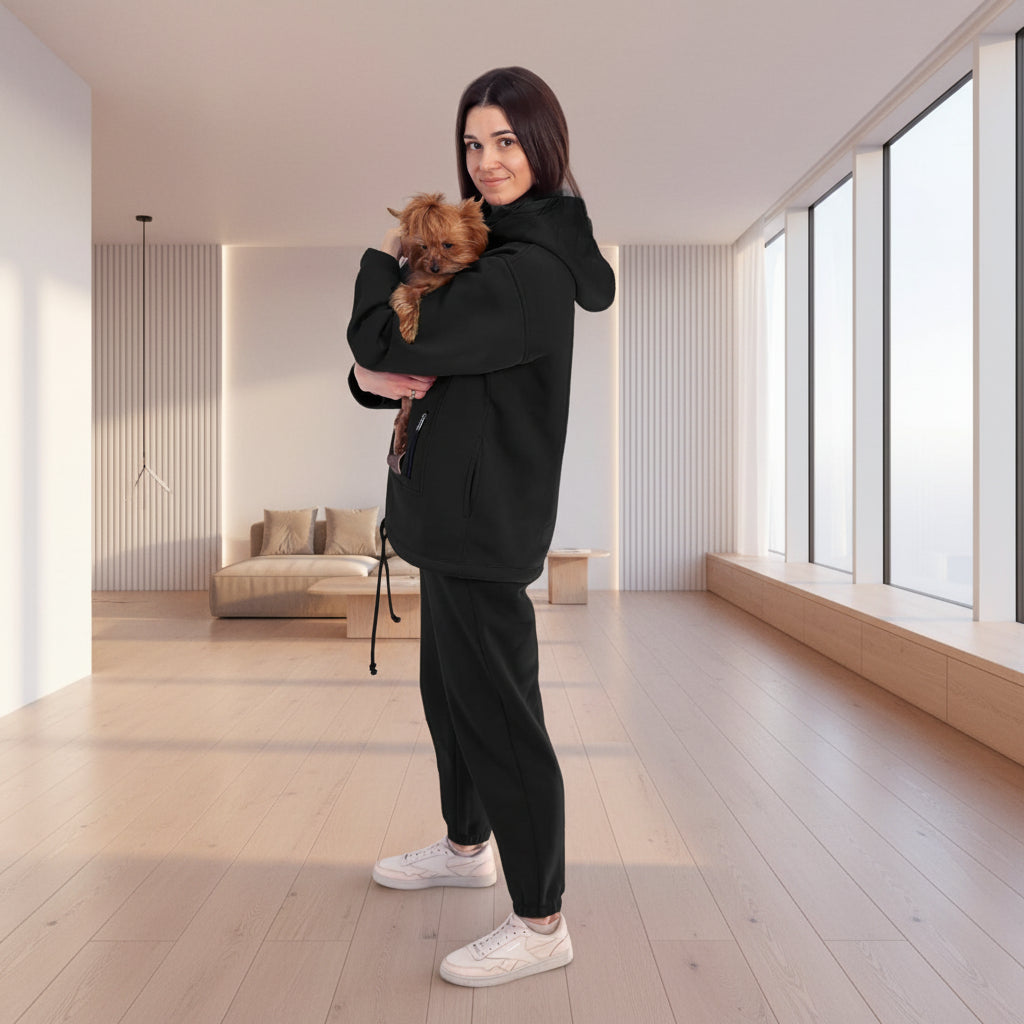 Woman in black tracksuit holding a small dog in a white room with plants.