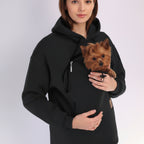 Person wearing a black hoodie holding a small brown dog.