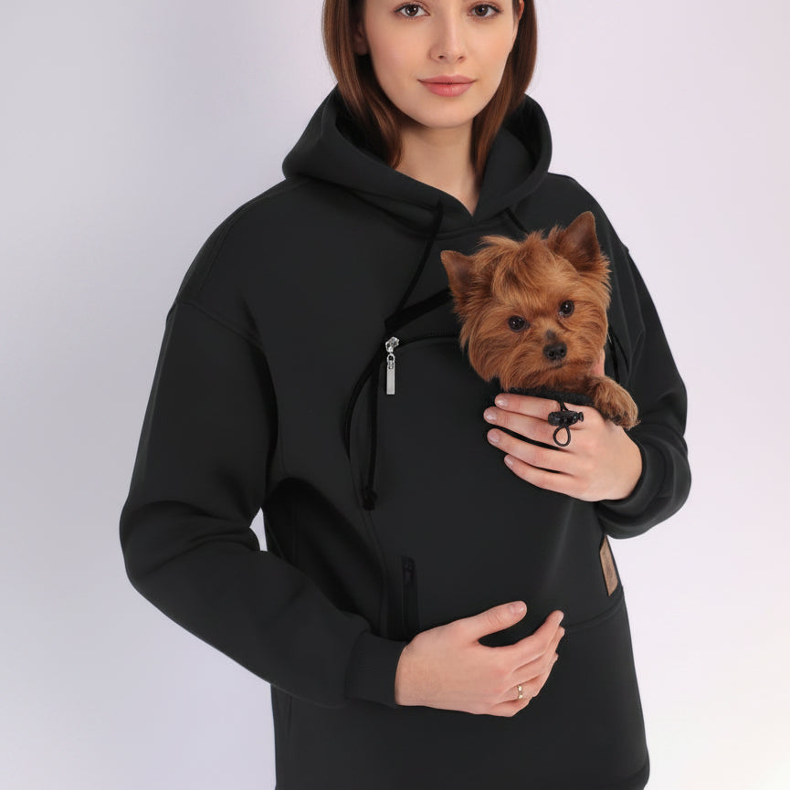 Person wearing a black hoodie holding a small brown dog.