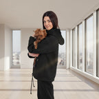 Woman in black tracksuit holding a small dog in a white room with plants.