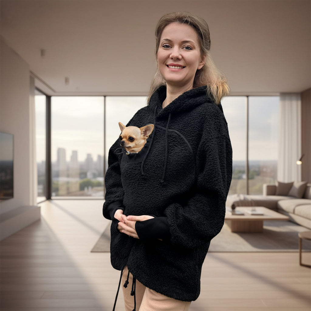 Woman holding a small dog in a black boucle hoodie in living room Main image