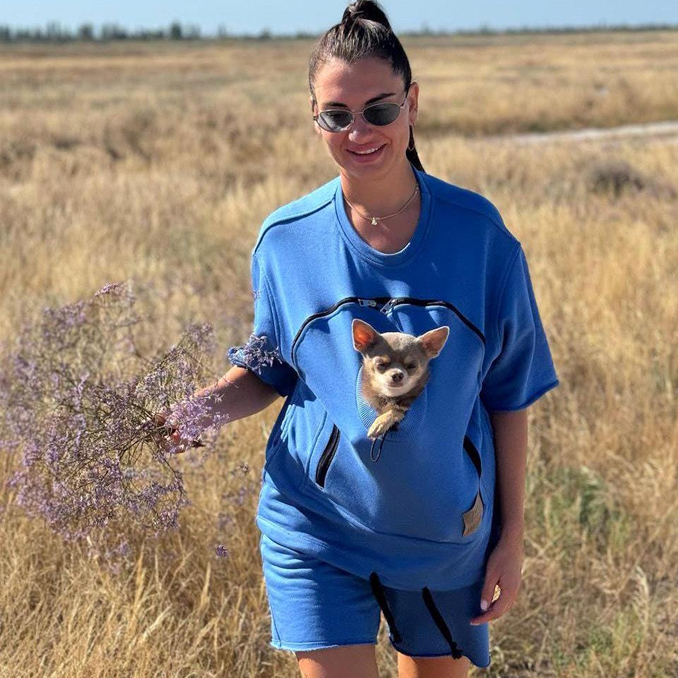 Woman in a blue t-shirt with a dog, holding a plant in a field