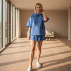 Woman in a blue outfit standing in a sunlit outdoor setting with columns in the background