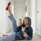 Woman wearing a dark blue denim hoodie with a cat in the front pouch in a room