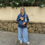 Girl wearing a dark blue denim hoodie with a cat in the front pouch against a garden background