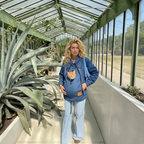 Woman wearing a dark blue denim hoodie with a cat in the front pouch against a garden background