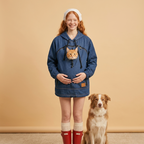 Woman wearing a dark blue denim hoodie with a cat in the pouch against a beige background.