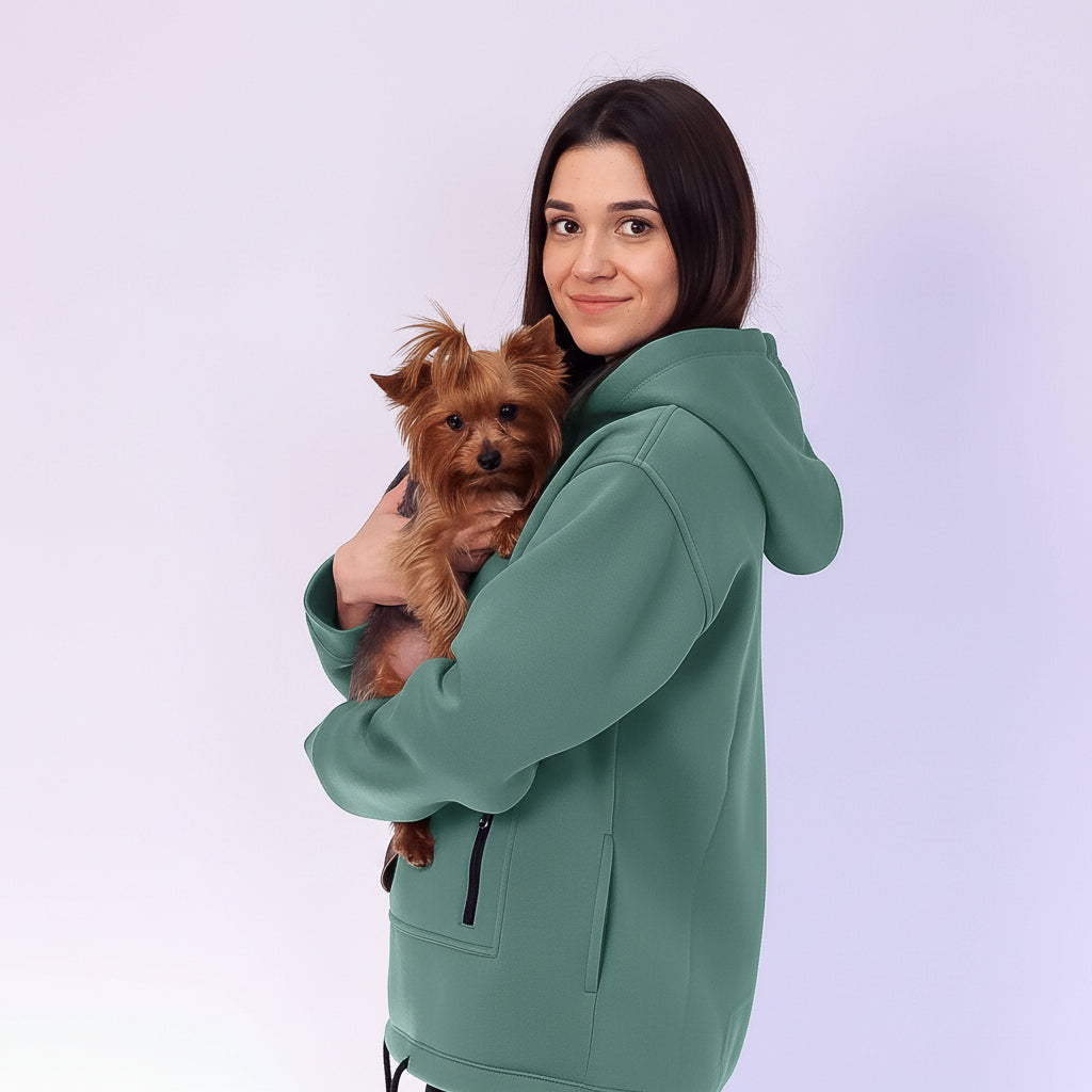 Woman wearing a emerald hoodie holding a small brown dog on a light purple background Main image