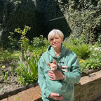 Person in a emerald  hoodie holding a small animal in a garden