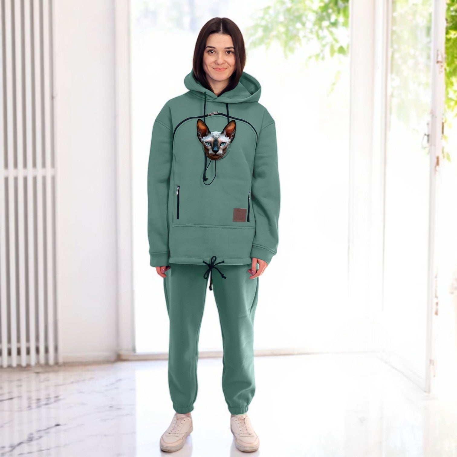 Person wearing a emerald hoodie and pants with a dog, standing in a bright room. Main image