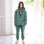 Person wearing a emerald hoodie and pants with a dog, standing in a bright room.