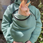 Person wearing a emerald hoodie with a small pouch over their shoulder, holding a Sphynx cat.