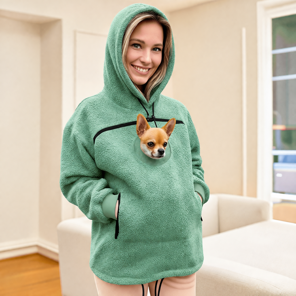 Person wearing a green hoodie with a dog peeking out of a pocket, sitting on a couch.