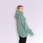Person wearing a green oversized hoodie on a light purple background