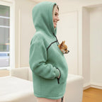 Person wearing a green fleece hoodie with a pocket, holding a small dog.