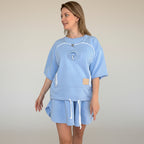 Woman wearing a light blue outfit with a logo on a plain background