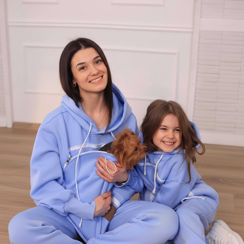 Woman and child in matching light blue hoodies with a small dog, sitting on a light-colored floor. Main image