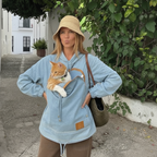 Woman wearing a light blue denim hoodie with a cat in the front pouch on a charming European street
