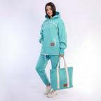 Person wearing a mint tracksuit with a matching tote bag on a white background